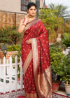 Woman wearing a maroon Banarasi silk saree with gold zari border, standing in a traditional outdoor setting