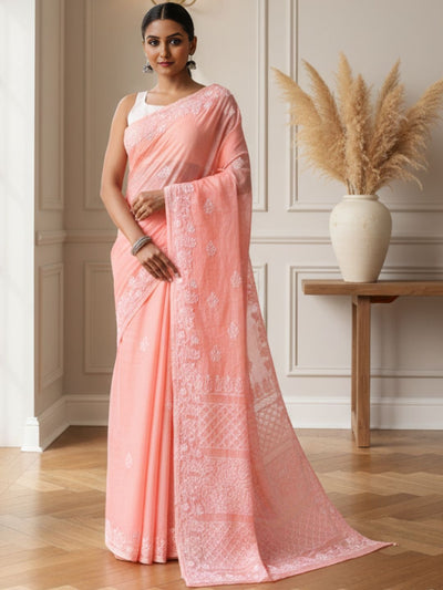 Woman wearing a pink saree with a white border in an indoor setting.